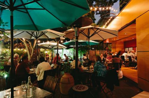 A cozy outdoor dining area with umbrellas, string lights, and patrons enjoying their meals in a warm evening atmosphere.