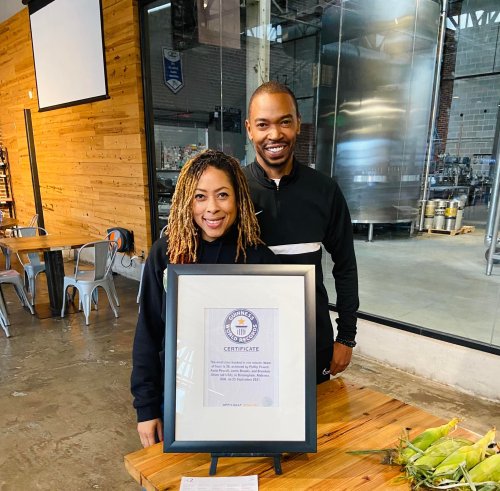 Two people stand behind a framed certificate in a spacious, modern venue with wooden walls and brewing equipment in the background.