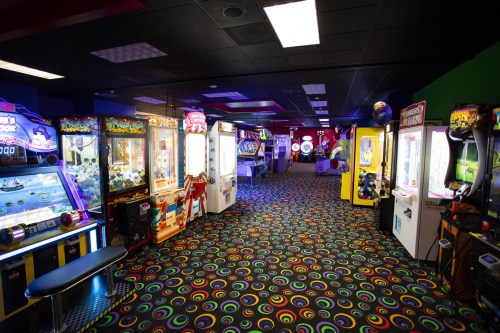 A colorful arcade with various game machines and a vibrant, patterned carpet.