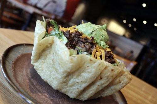 A taco salad in a crispy tortilla bowl, filled with beef, lettuce, cheese, and guacamole on top.