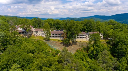 Aerial view of a hillside resort surrounded by lush greenery and mountains under a partly cloudy sky.