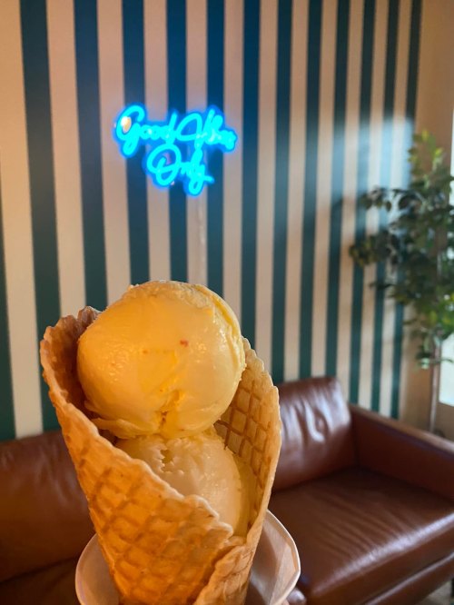 A close-up of a waffle cone with two scoops of ice cream, with a neon sign and striped wall in the background.