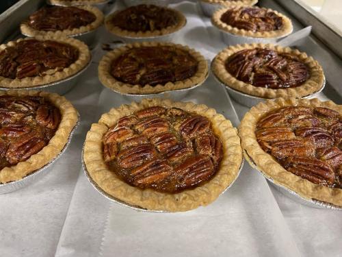 A tray of freshly baked pecan pies in individual aluminum crusts, arranged neatly on parchment paper.