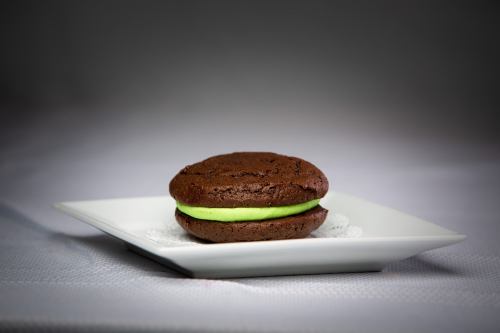 A chocolate whoopie pie with a bright green filling, presented on a white plate.