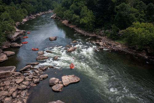 Aerial view of a river with rocky banks and several rafts navigating the rapids amidst lush green trees.