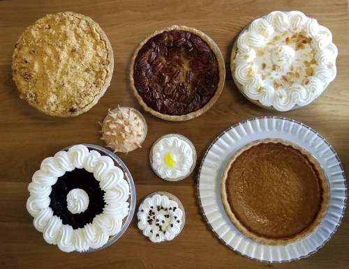 A variety of desserts including pies and cakes topped with whipped cream, arranged on a wooden table.