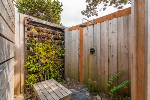Outdoor shower area with wooden walls, a vertical garden, and a small bench surrounded by greenery.