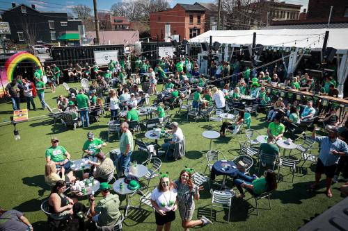 A lively outdoor gathering with people in green attire celebrating, surrounded by tables and festive decorations.