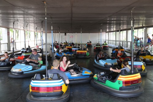 A lively bumper car arena with people enjoying rides in colorful cars, surrounded by spectators.