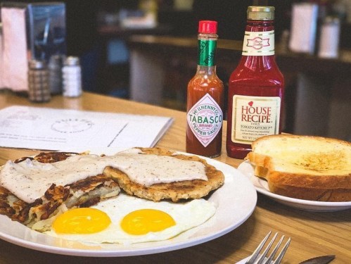 A plate of breakfast featuring eggs, hash browns, sausage gravy, toast, and bottles of Tabasco and ketchup.