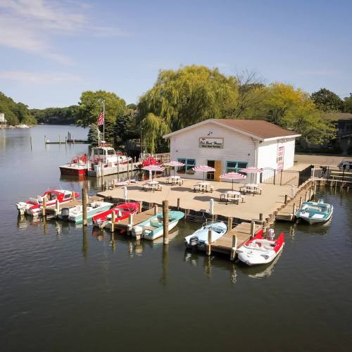 Aerial view of a lakeside dock with colorful boats and a restaurant surrounded by trees and water.