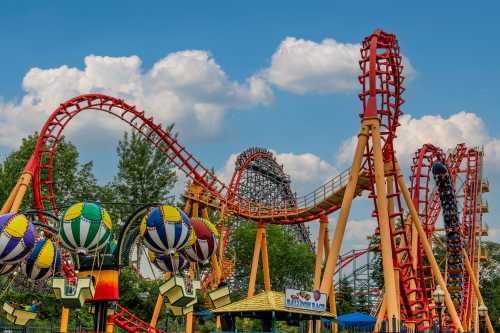 A vibrant amusement park scene featuring colorful roller coasters and hot air balloon rides under a blue sky.