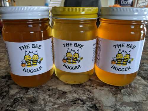 Three jars of honey with labels featuring cartoon bees and the text "The Bee Hugger" on a granite countertop.
