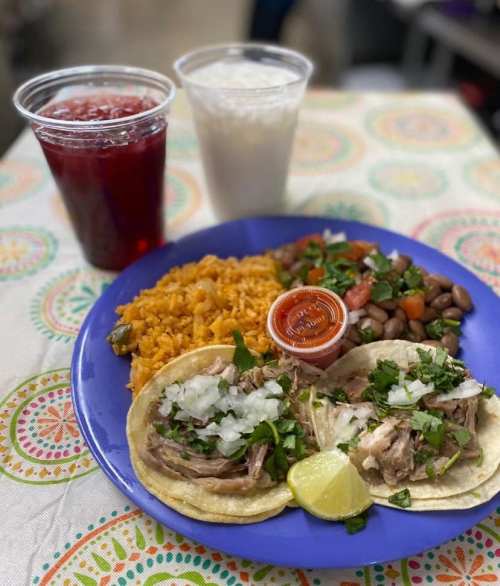 A blue plate with two tacos topped with meat, onions, and cilantro, served with rice, beans, salad, and drinks.