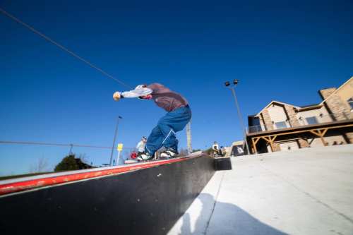 A skateboarder performs a trick on a rail at a skate park under a clear blue sky.