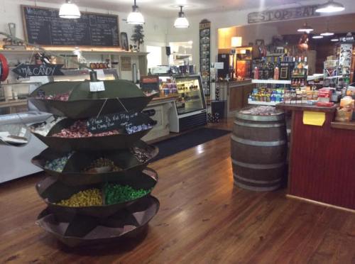 A cozy shop interior featuring a candy display, wooden barrel, and shelves filled with various goods.