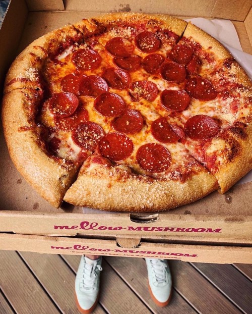 A pepperoni pizza in a Mellow Mushroom box, with a pair of sneakers visible below.