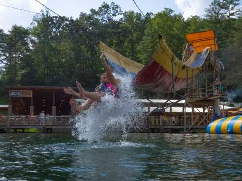 A person splashes into the water while jumping from a zipline at a lakeside recreation area. Trees and a platform are visible.