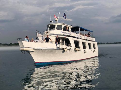 A white boat named "Haven Lady" on calm water, with people enjoying the view under a cloudy sky.