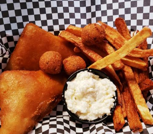 A plate of fried fish, hushpuppies, and crispy fries served in a checkered paper basket.