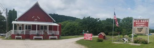 A red barn-style building with a sign for Red Barn Resort Camp, surrounded by greenery and a flagpole.