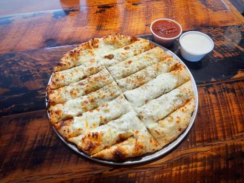 A round pizza with cheese and sliced into strips, served with marinara and ranch dipping sauces on a wooden table.
