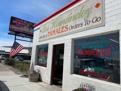 Exterior of Los Hernandez Tamales, featuring a colorful sign and an American flag, with a billboard in the background.
