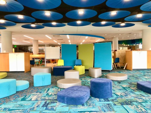 A modern library space with colorful seating, circular cushions, and partitioned areas for study and collaboration.