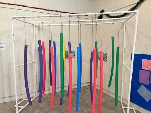 Colorful pool noodles hang from a white frame, creating a playful and vibrant display in a spacious indoor area.