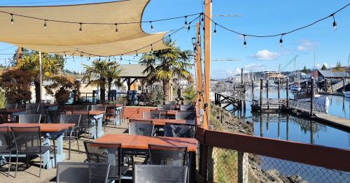 Outdoor dining area with tables, palm trees, and a view of a marina under a blue sky with string lights.