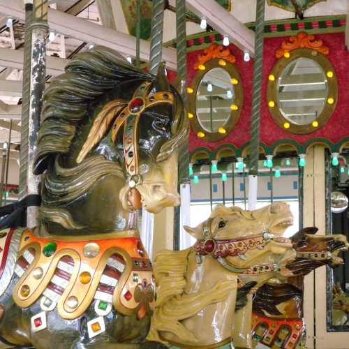 A close-up of ornate carousel horses with colorful decorations and mirrors in the background.