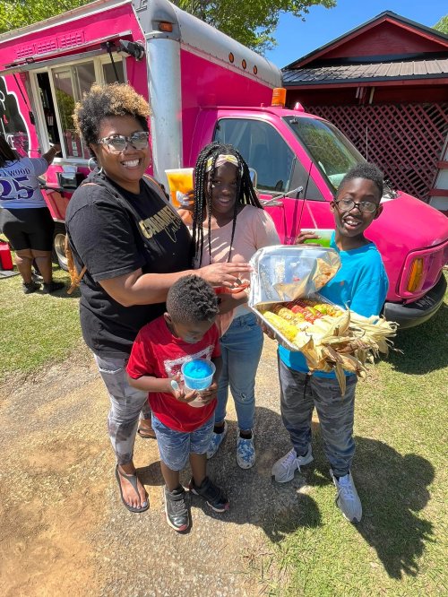 A group of four people, including two children, happily holding snacks in front of a colorful food truck.