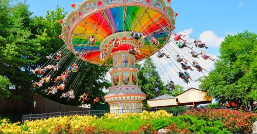 A colorful swing ride at an amusement park, with people enjoying the view against a backdrop of trees and blue sky.