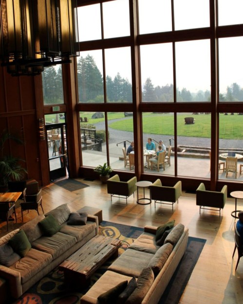 A spacious lobby with large windows, cozy seating, and a view of people dining outside on a grassy area.