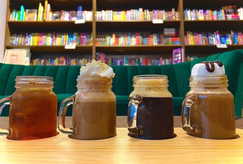 Four jars of coffee drinks with varying textures and toppings, set against a backdrop of colorful bookshelves.