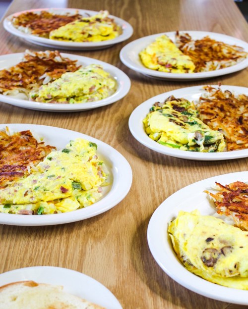 A table with several plates of omelets and crispy hash browns arranged neatly on a wooden surface.