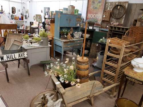A cozy antique shop filled with vintage furniture, decor, and rustic items, including a wheelbarrow and wooden barrels.