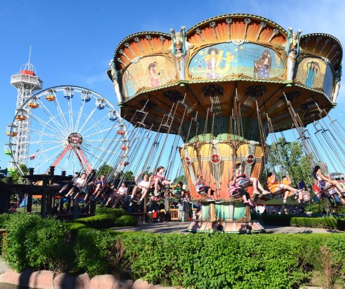 A vibrant amusement park scene featuring a swing ride and a Ferris wheel against a clear blue sky.