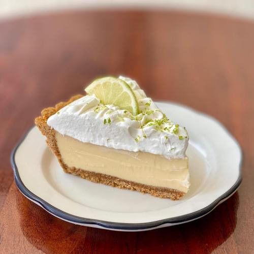 A slice of key lime pie topped with whipped cream and a lime wedge, served on a white plate with a blue rim.