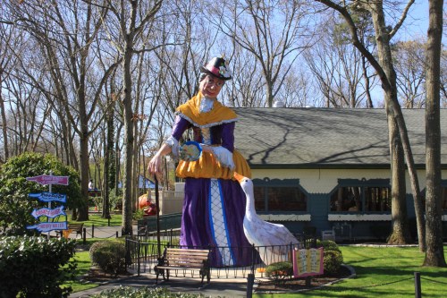 A large, colorful statue of a woman in a dress stands in front of a building, surrounded by trees and greenery.