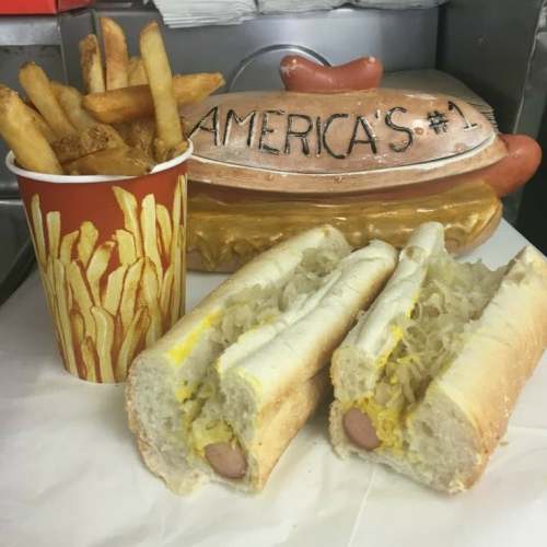 A plate with two hot dogs topped with mustard and sauerkraut, alongside a cup of fries and a decorative hot dog container.