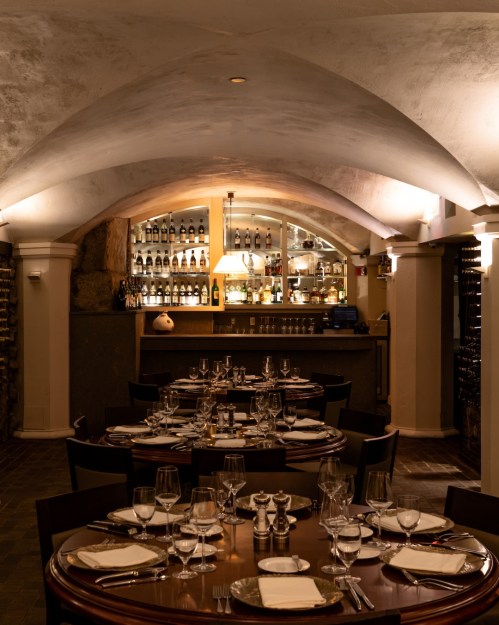 Elegant restaurant interior with arched ceilings, a round table set for dining, and a well-stocked bar in the background.