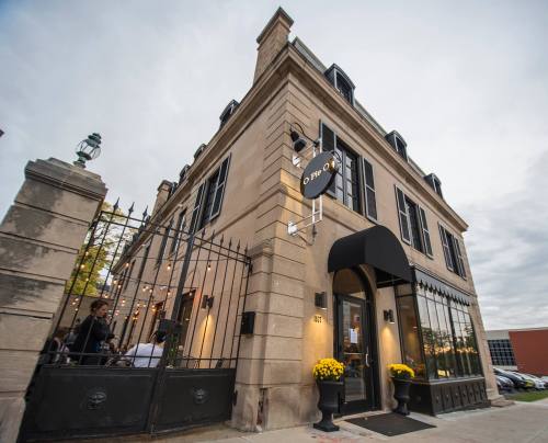 Exterior of a stylish restaurant with a black awning, large windows, and yellow flowers, set against a cloudy sky.