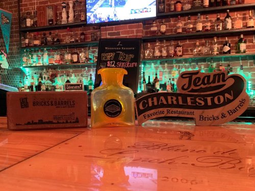 A bar scene featuring a bottle of yellow drink, a sign for Team Charleston, and a menu for Bricks & Barrels.