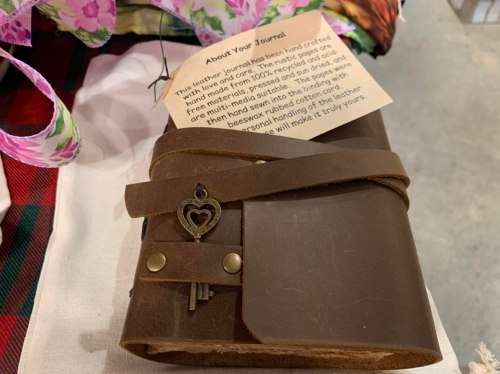 A handcrafted leather journal with a heart-shaped key charm, accompanied by an informational card about its creation.