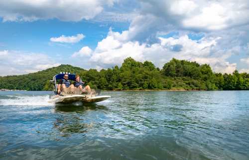 Two people enjoy a boat ride on a lake, surrounded by lush greenery and a partly cloudy sky.