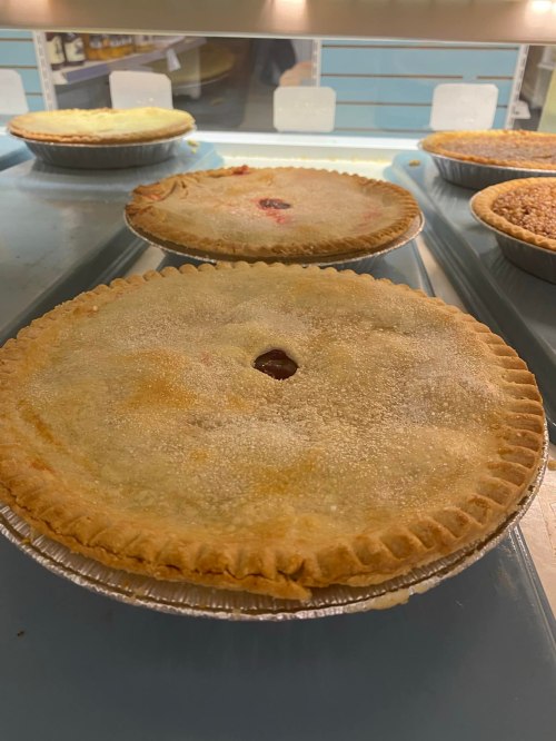Two freshly baked pies with golden crusts, displayed on a blue surface in a bakery setting.