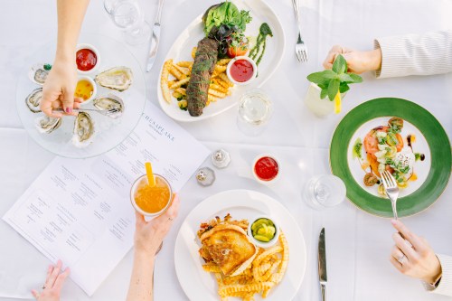 A table set with various dishes, including oysters, a steak, and fried chicken, alongside drinks and a menu.