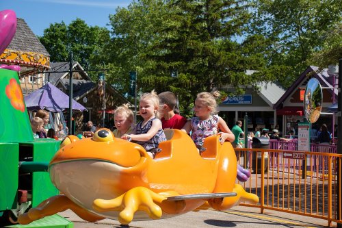 Children enjoy a colorful frog-themed amusement ride at a lively outdoor park on a sunny day.