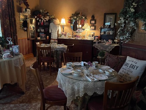 Cozy tea room with elegantly set tables, vintage decor, and a display of teacups and collectibles.